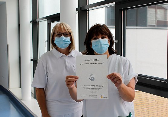 Steffi John und Katharina Blessin (v.l.n.r.), Fachschwestern f&uuml;r Krankenhaushygiene, pr&auml;sentieren das Silber-Zertifikat der Aktion Saubere H&auml;nde. (Foto: Helios Kliniken Mansfeld-S&uuml;dharz)
