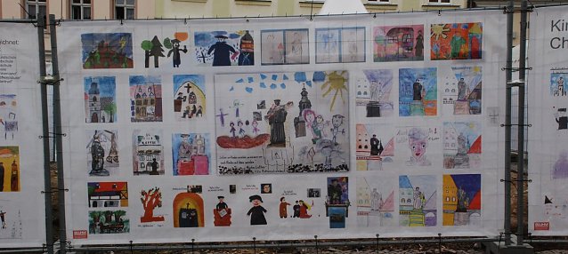 Bild: Kinder aus Eisleber Einrichtungen malten Bilder zum Thema "Martin Luther". Auf drei Planen am Bauzaun rund um den Standort des Lutherdenkmals werden diese Bilder nun gezeigt.