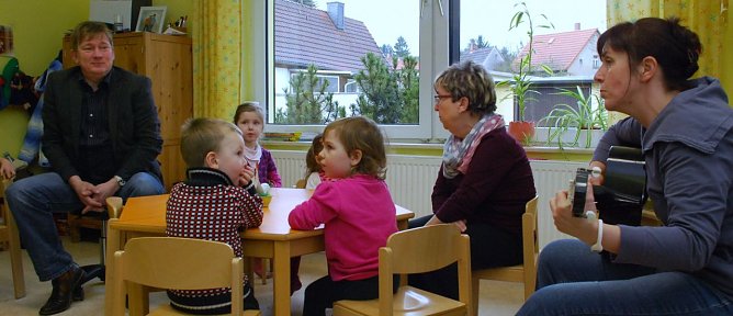 Ganz spontan nahm Erzieherin Katrin Steinbr&uuml;ck die Gitarre und sang gemeinsam mit den Kindern den G&auml;sten Lieder vor. Vorher hatte Norbert Born mit zwei Liedern &uuml;berrascht. Die Erzieherin am Fenster ist Elisabeth Liener. (Foto: Jochen Miche)
